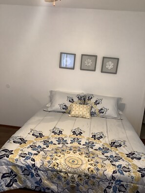 A bedroom with a bed, floral-patterned bedding, and three framed pictures on the wall.
