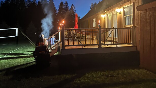 Een houten gebouw met terras, buiten zitplaatsen en een schoorsteen waar rook uit komt.