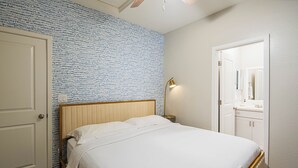 Une chambre à coucher avec un lit, une table de chevet, une lampe, une porte et un mur orné d’un motif bleu.