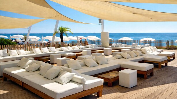 Un espace de détente aménagé au bord de la plage, offrant de nombreuses options d’assises, notamment des canapés et des fauteuils, le tout abrité sous de grands auvents.