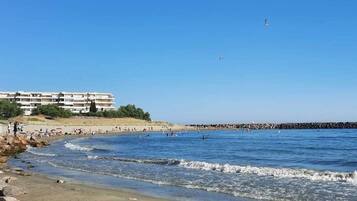 Une plage bordée d’une côte rocheuse, avec une jetée et un bâtiment doté de nombreux balcons.