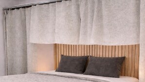 Un lit avec une tête de lit en bois, une literie grise et un rideau.
