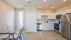 Una cocina moderna con armarios blancos, electrodomésticos de acero inoxidable y una mesa de comedor de vidrio.