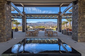 Una terrazza esterna con piscina rettangolare, colonne in pietra e vista sulle montagne.