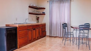 Une cuisine compacte équipée d’un réfrigérateur, de meubles en bois, d’un évier et d’un coin repas avec des chaises en métal.