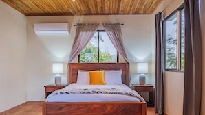 Une chambre à coucher avec un lit en bois, deux tables de chevet, une fenêtre avec des rideaux et un appareil de climatisation.