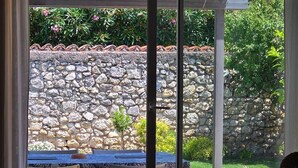 Et værelse med en skydedør, der fører til en udendørs terrasse med en stenvæg, en pool og plantekasser.