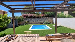 En baghave med swimmingpool, pergola, stenvæg og træterrasse.