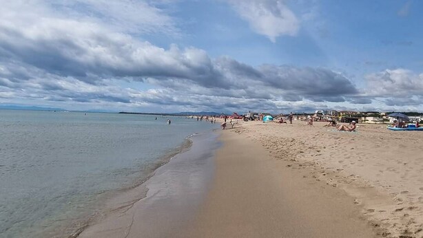 En bred, sandet strand med klart vand og let overskyet himmel.