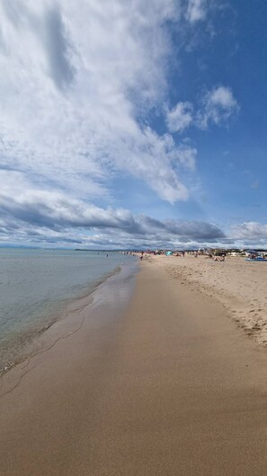 Uma extensa praia de areia com águas cristalinas e céu parcialmente nublado.