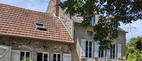 Une maison de campagne à l’aspect rustique, avec une façade en pierre, un toit en tuiles et une petite fenêtre.