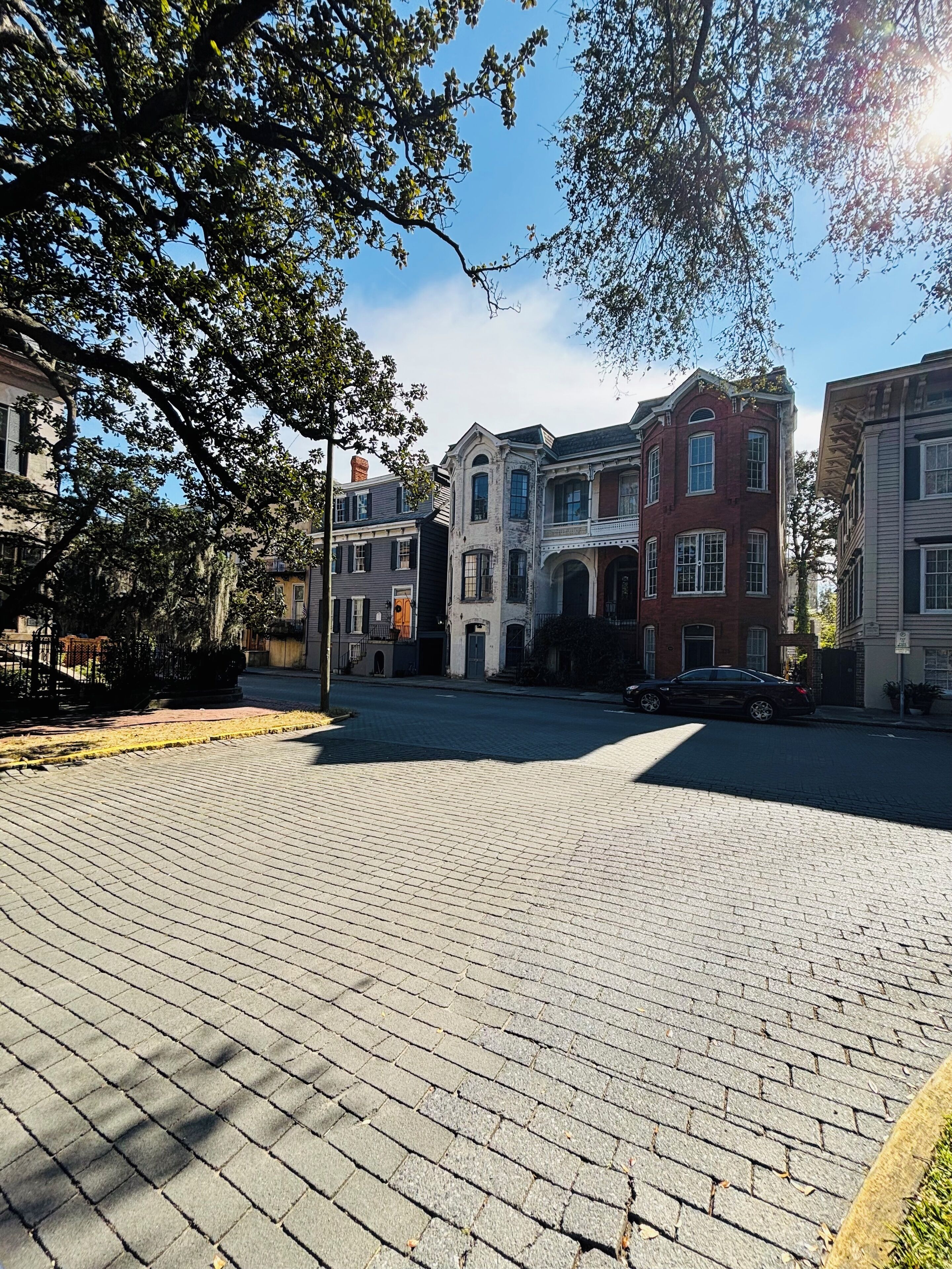 Una plaza empedrada con edificios históricos, un coche y árboles.