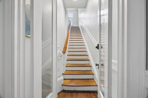 A staircase with white walls and wooden steps leading to a landing. - Henry Hayme House Penthouse: Overlooking Orleans Square (Savannah)