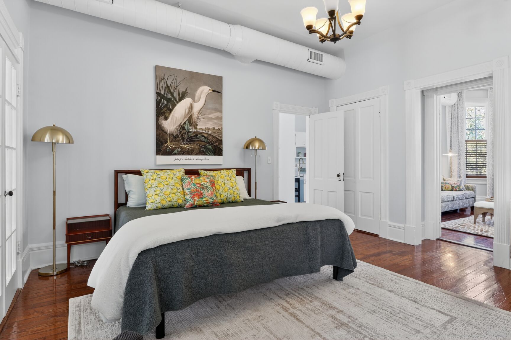 A bedroom with a bed, a large painting of a bird, and a chandelier.