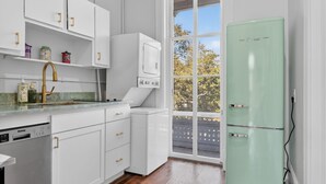 A kitchen with white cabinets, a Danby dishwasher, a green refrigerator, and a window with a view of trees. - Henry Hayme House Penthouse: Overlooking Orleans Square (Savannah)