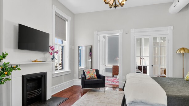 A bedroom with a fireplace, a bed, a TV, and a large window. - Henry Hayme House Penthouse: Overlooking Orleans Square (Savannah)