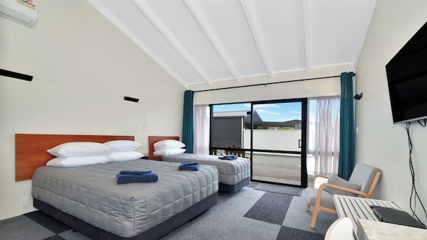 A hotel room with two beds, a desk, a chair, a TV, and a sliding glass door to the outside.