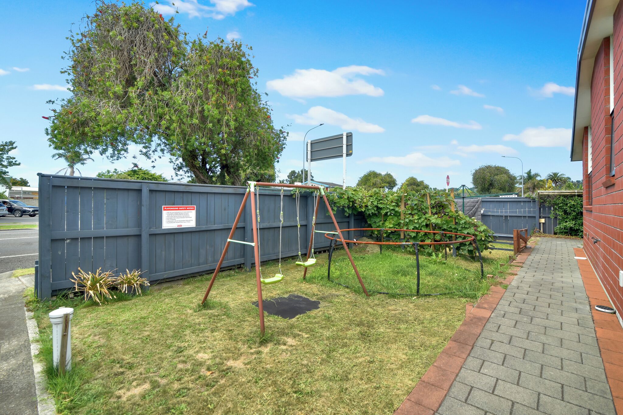 A fenced yard with a swing set, a brick pathway, and a red building.