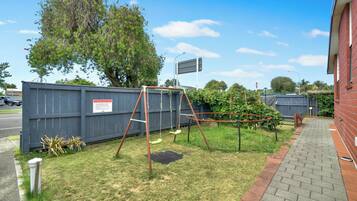 A fenced yard with a swing set, a brick pathway, and a red building.