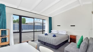 A modern hotel room with a large bed, a sofa, a desk, and a view of the outside.
