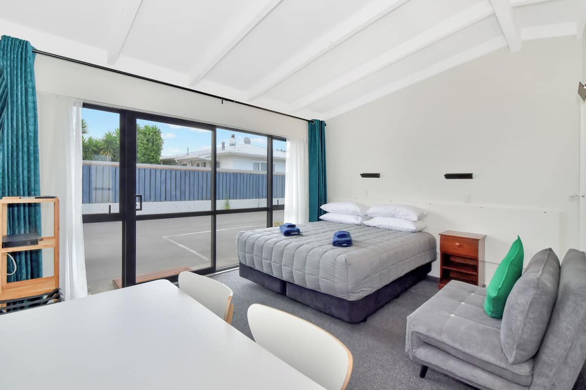 A modern hotel room with a large bed, a sofa, a desk, and a view of the outside.