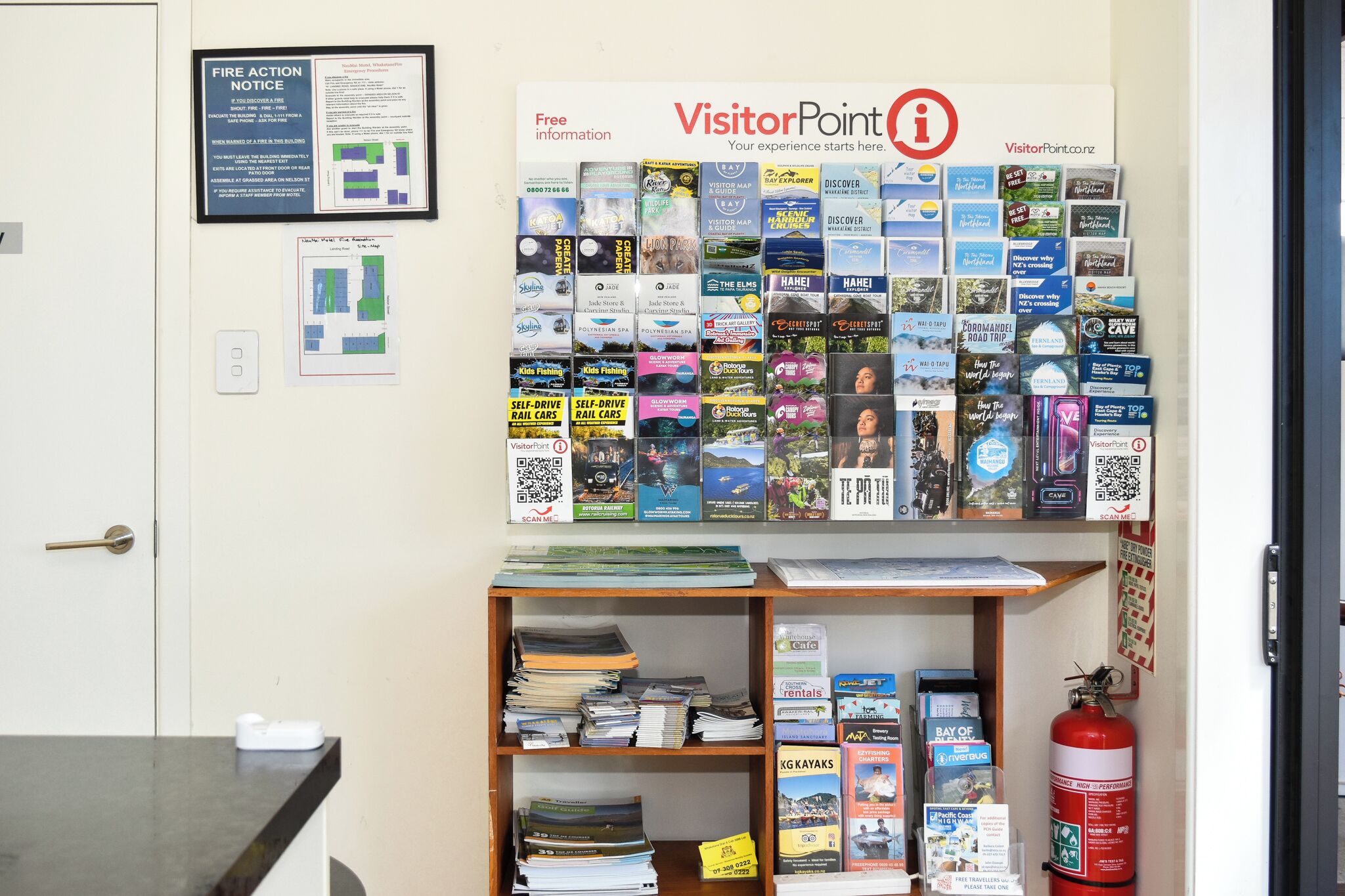 A bulletin board with various travel brochures and a fire action notice.