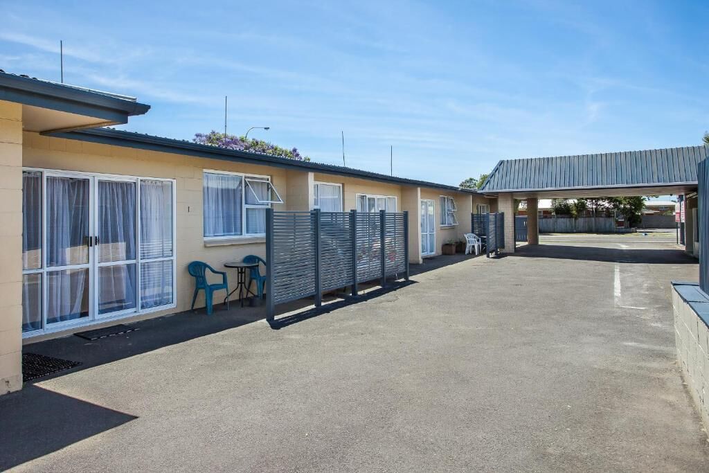 Un motel doté d’un parking couvert, d’un espace extérieur aménagé avec une clôture et d’un bâtiment comportant de nombreuses fenêtres.