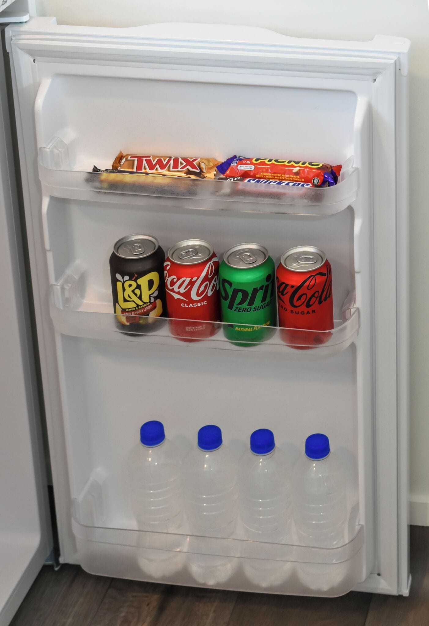 Un mini-frigorifero con L&P, Coca-Cola, Sprite e una confezione di Twix.