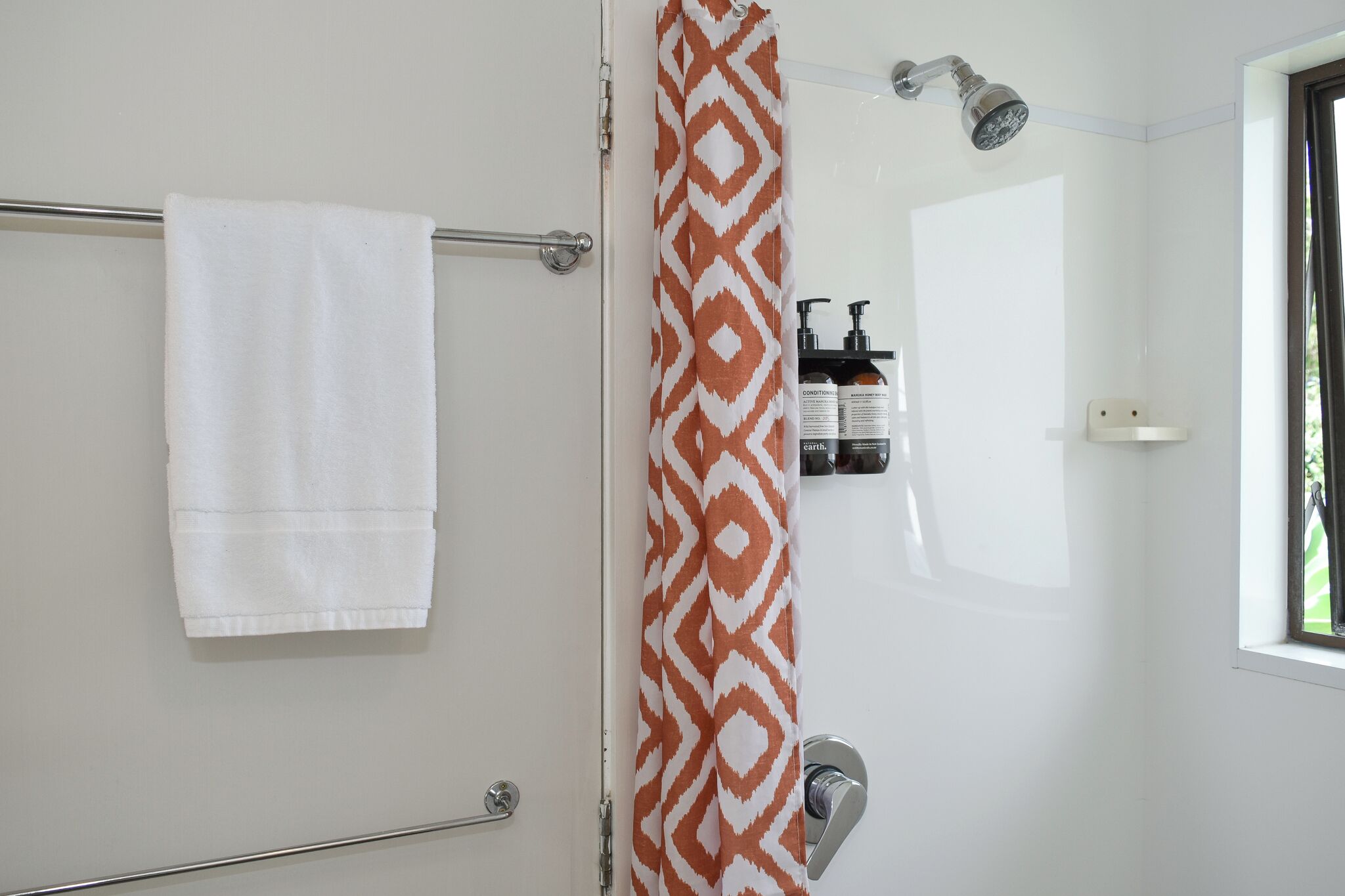 A bathroom with a white towel hanging on a rack, a shower with a patterned curtain, and a window providing natural light.