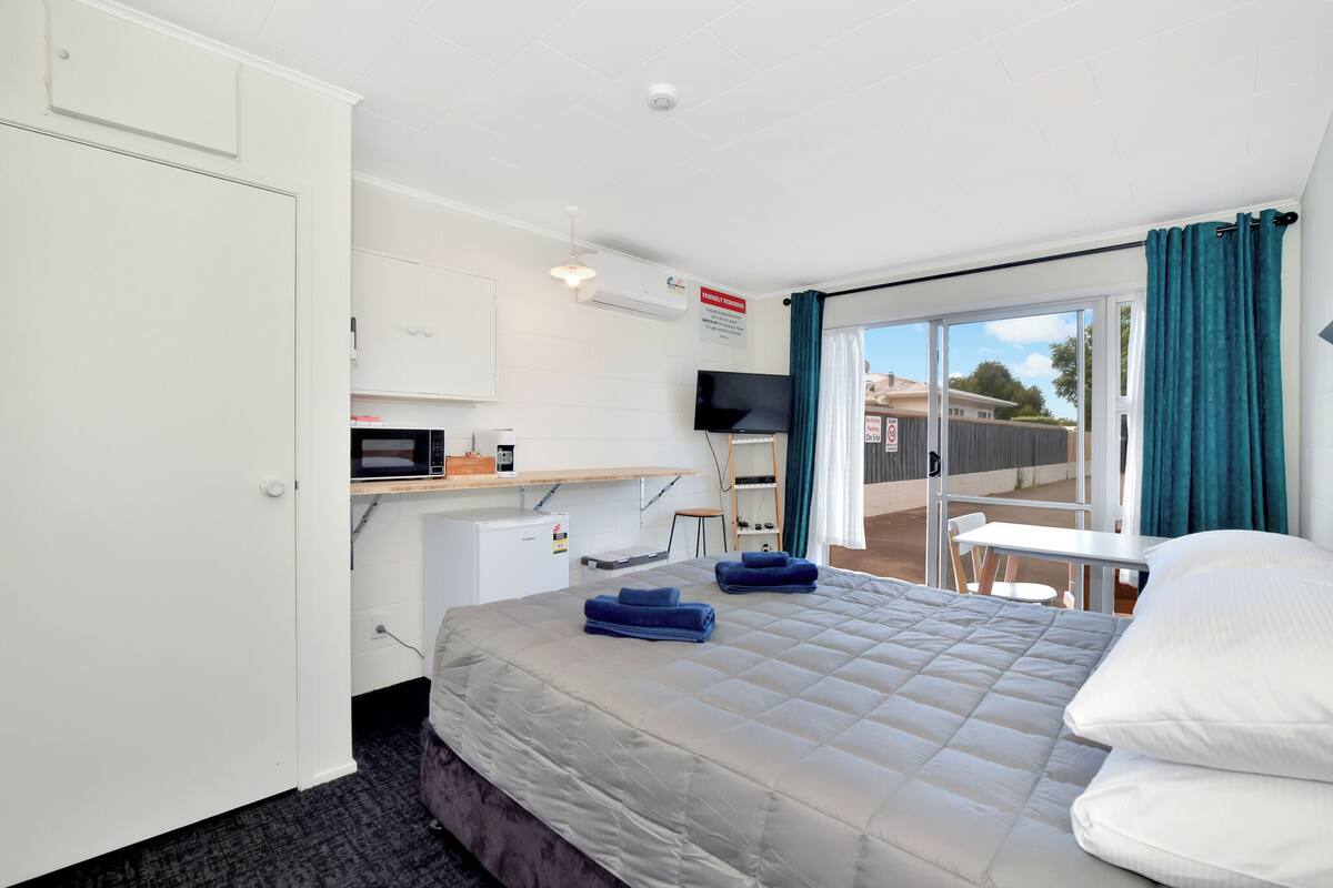 A hotel room with a bed, a desk, a microwave, a television, and a sliding glass door to the outside.