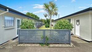 A row of single-story mobile homes with a central pathway, surrounded by greenery and a metal fence.