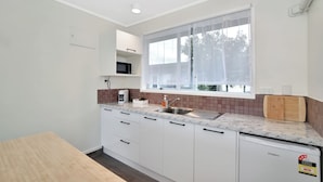A modern kitchen with white cabinets, a marble countertop, a sink, and a window with sheer curtains.