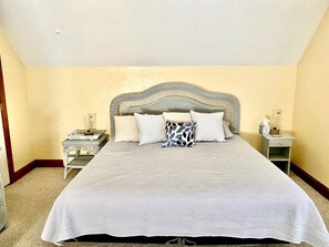 Una cama bien hecha con colcha blanca, cabecera gris y dos mesitas de noche con lámparas.