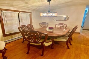 Un comedor con una mesa de madera, seis sillas, una lámpara de araña y un espejo en la pared.
