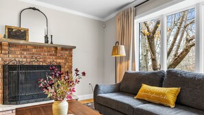 Ein Wohnzimmer mit Kamin aus Backsteinen, einer Couch mit Kissen, einem Couchtisch aus Holz und einem Fenster mit Vorhängen.
