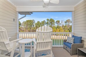 A covered porch with white chairs, a wicker sofa, and a view of a beach and trees. - 2 BR Barefoot Resort Getaway - Free Shuttle to Beach - 2 Pools  (North Myrtle Beach)