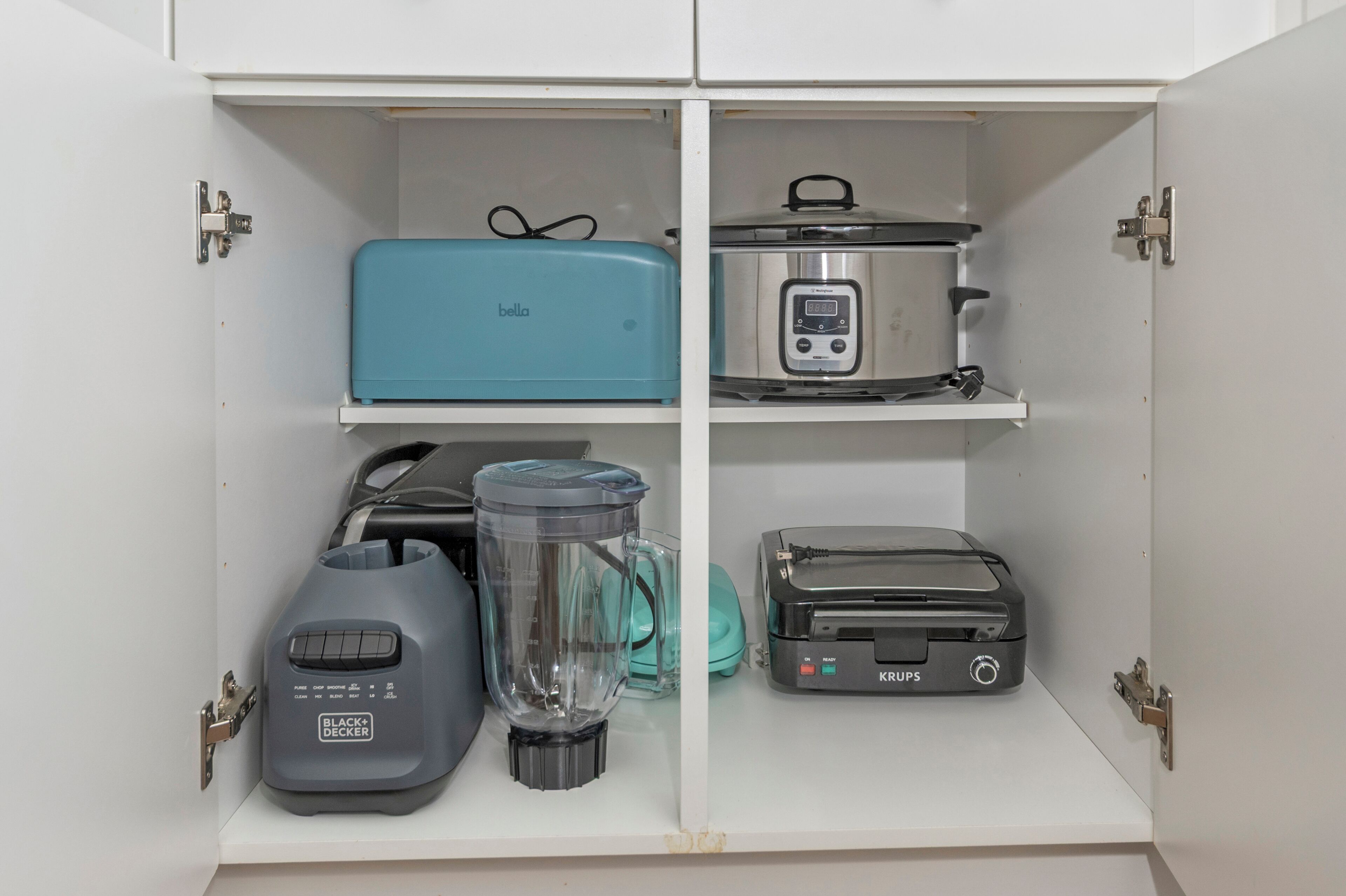 Een keukenkastje met een blauw apparaat, een roestvrijstalen slowcooker, een blender en een broodrooster.