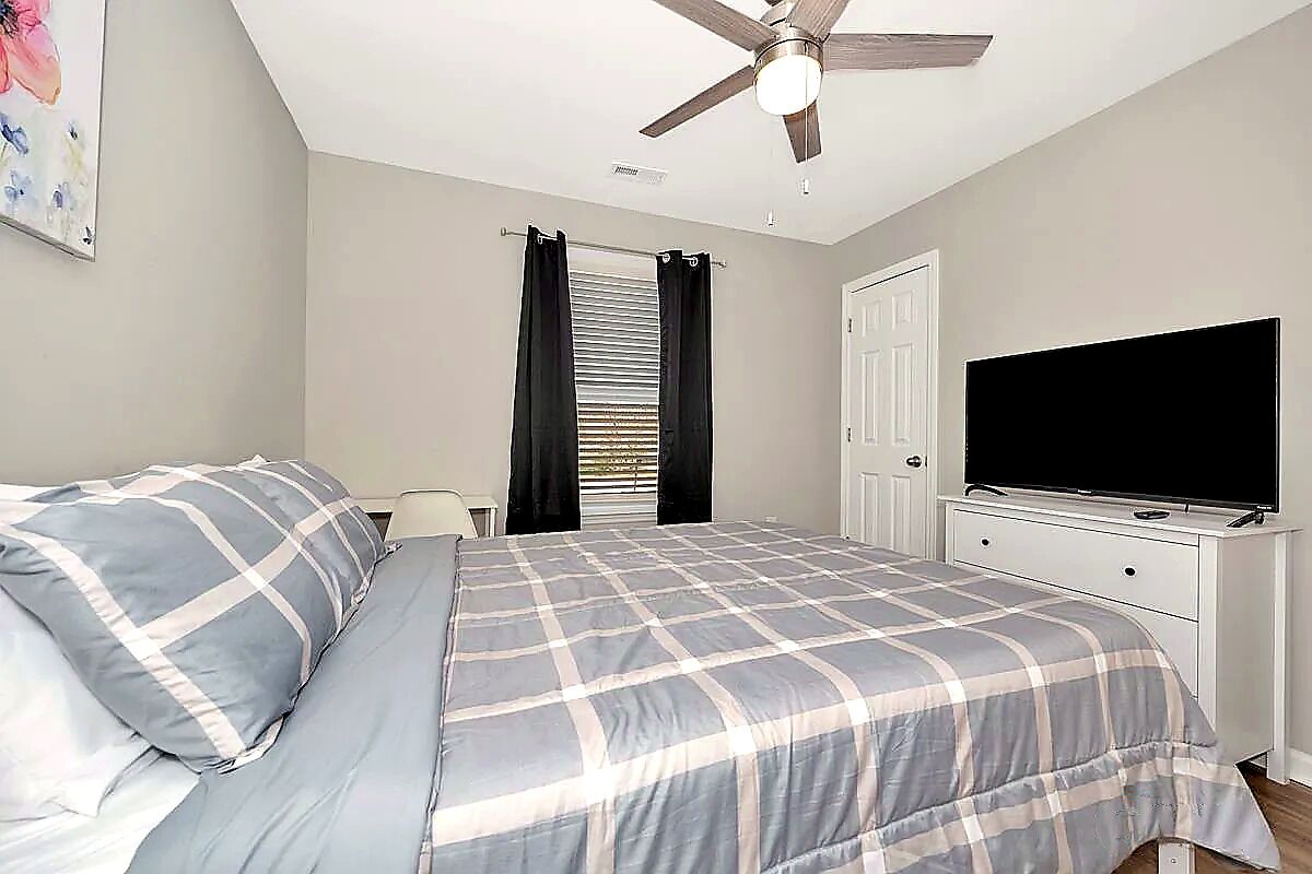 A bedroom with a bed, a ceiling fan, a TV, and a door.