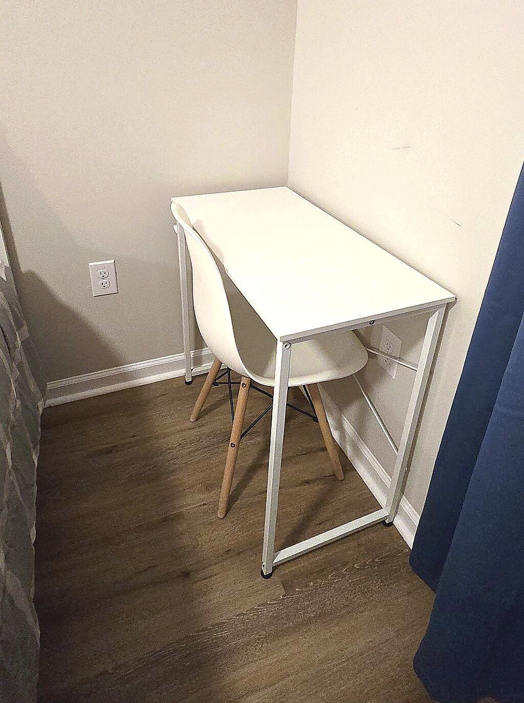 Habitación de esquina con un escritorio blanco, una silla y piso de madera.