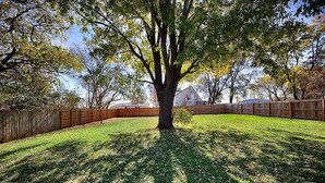 A large tree in a backyard with a wooden fence and houses in the background. - Modern 2BR/2BA Home. Large Backyard. 5 Gig Fiber. Nr VBC, Arsenal & Space Center (Huntsville)