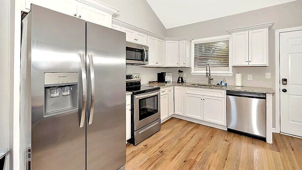A modern kitchen with stainless steel appliances, white cabinetry, and a wooden floor. - Modern 2BR/2BA Home. Large Backyard. 5 Gig Fiber. Nr VBC, Arsenal & Space Center (Huntsville)