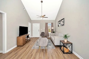 A living room with a ceiling fan, a TV, a sofa, a coffee table, and a side table with a plant.