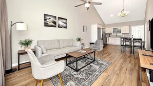 A modern living room with a sofa, coffee table, and chairs, a kitchen in the background, and a ceiling fan. - Modern 2BR/2BA Home. Large Backyard. 5 Gig Fiber. Nr VBC, Arsenal & Space Center (Huntsville)