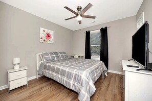 Une chambre à coucher comprenant un lit, une table de chevet, un bureau, un ventilateur de plafond et un téléviseur.