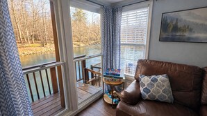 A room with a view of a river, a wooden deck, a brown leather sofa, and a small table with books. - Cozy 1-bedroom cabin in serene Ellijay (Ellijay)