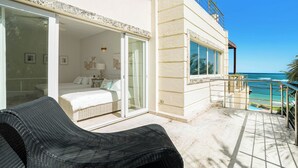 A hotel room with a balcony, a bed, a sitting area, and a view of the ocean. - Beachfront Luxury Penthouse w/ Ocean Views (Cabarete)