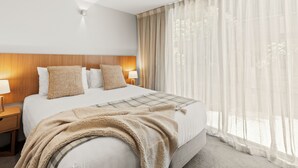 Ett hotellrum med en stor säng, två sängbord med lampor, en träpanel som huvudgavel, tunna gardiner och utsikt över omgivningarna.