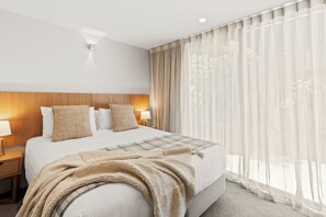 Ein Hotelzimmer mit einem großen Bett, zwei Nachttischen mit Lampen, einem Holzkopfstück, transparenten Vorhängen und Blick ins Freie.