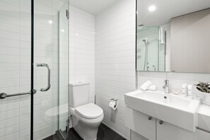 Ein modernes Badezimmer mit Duschkabine aus Glas, einer weißen Toilette und einem Waschbecken mit Pflegeprodukten.