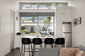 Eine moderne Küche mit großem Fenster, Einbauherd und Kühlschrank. Vier schwarze Barhocker und ein graues Sofa mit einem flauschigen Überwurf.